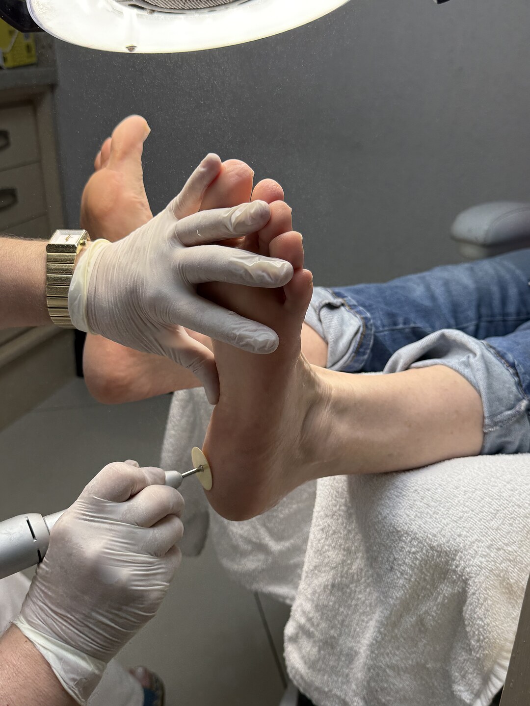 Podóloga com luvas brancas removendo calosidade do pé de cliente com ferramenta elétrica, sobre toalha branca, no Nix Beauty Salon, no Shopping Palladium, em Curitiba