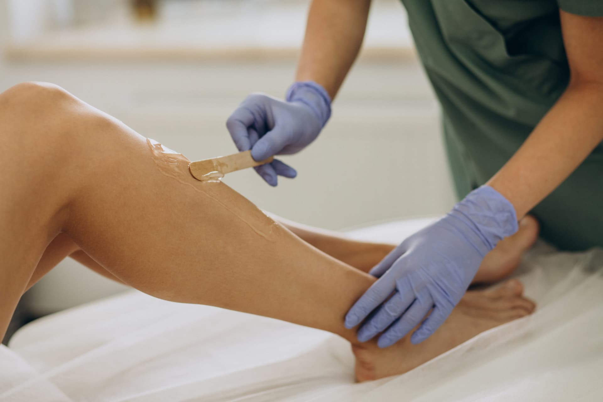 Profissional de luvas aplicando cera com espátula na perna de cliente, depilação feita no Nix Beauty Salon, no Shopping Palladium, em Curitiba