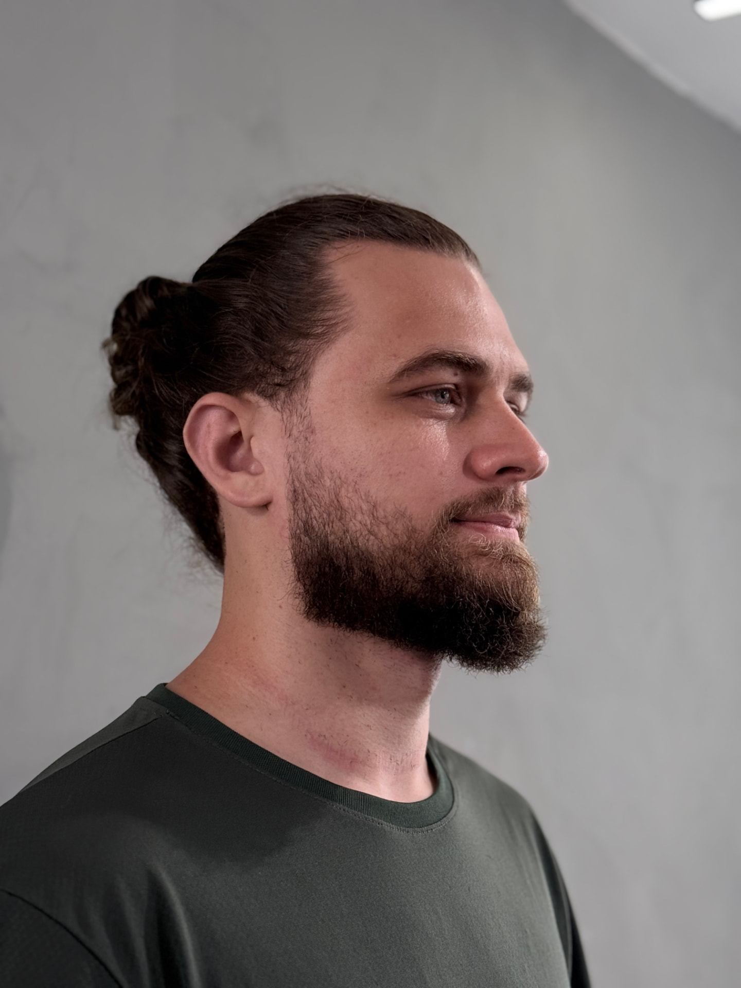 Cliente com barba modelada e cabelo longo preso em coque, na Nix Barbearia, no Shopping Palladium, em Curitiba