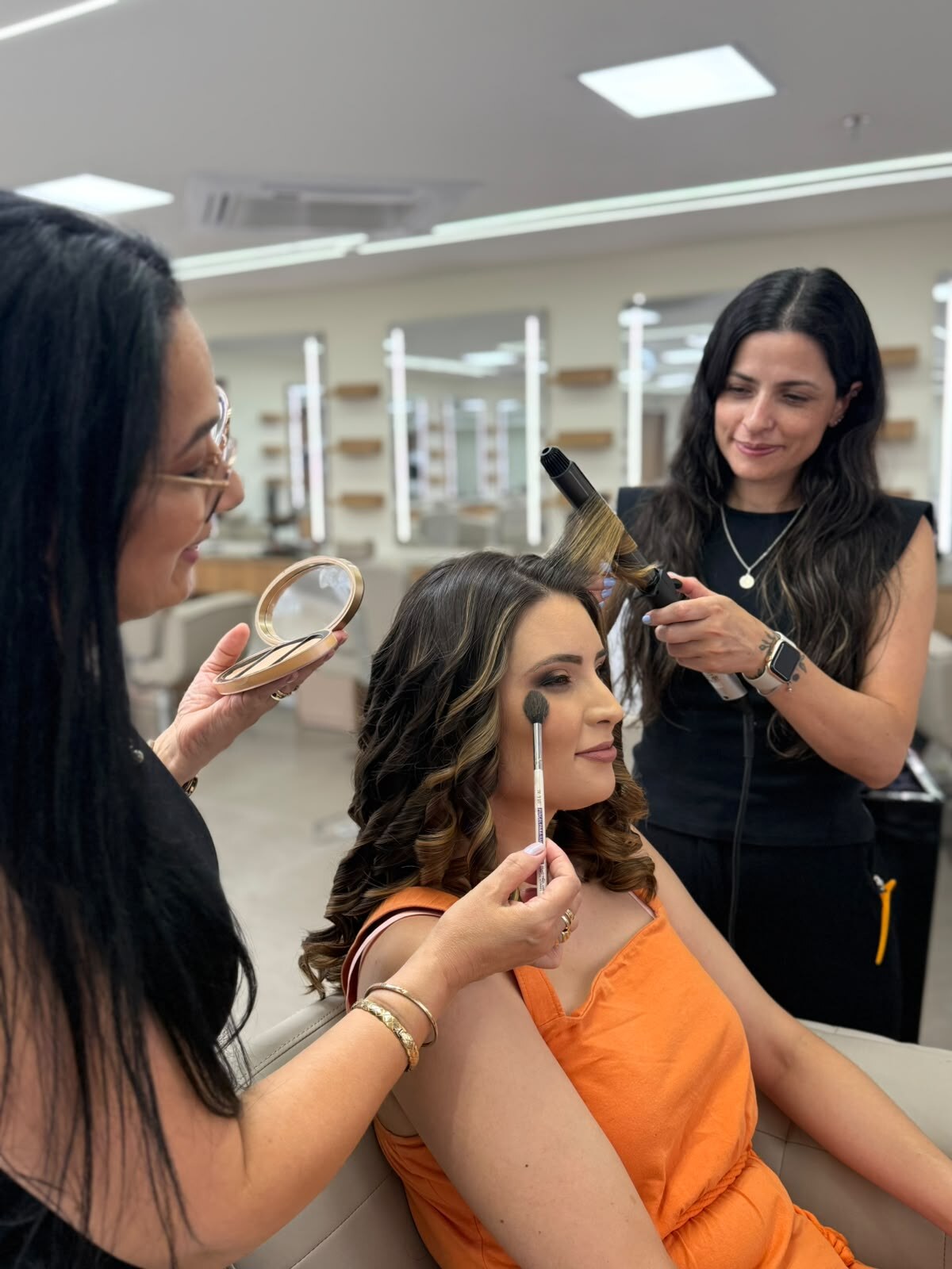 Cliente recebendo maquiagem e cachos ao mesmo tempo, com duas profissionais do Nix Beauty Salon, no Shopping Palladium, em Curitiba