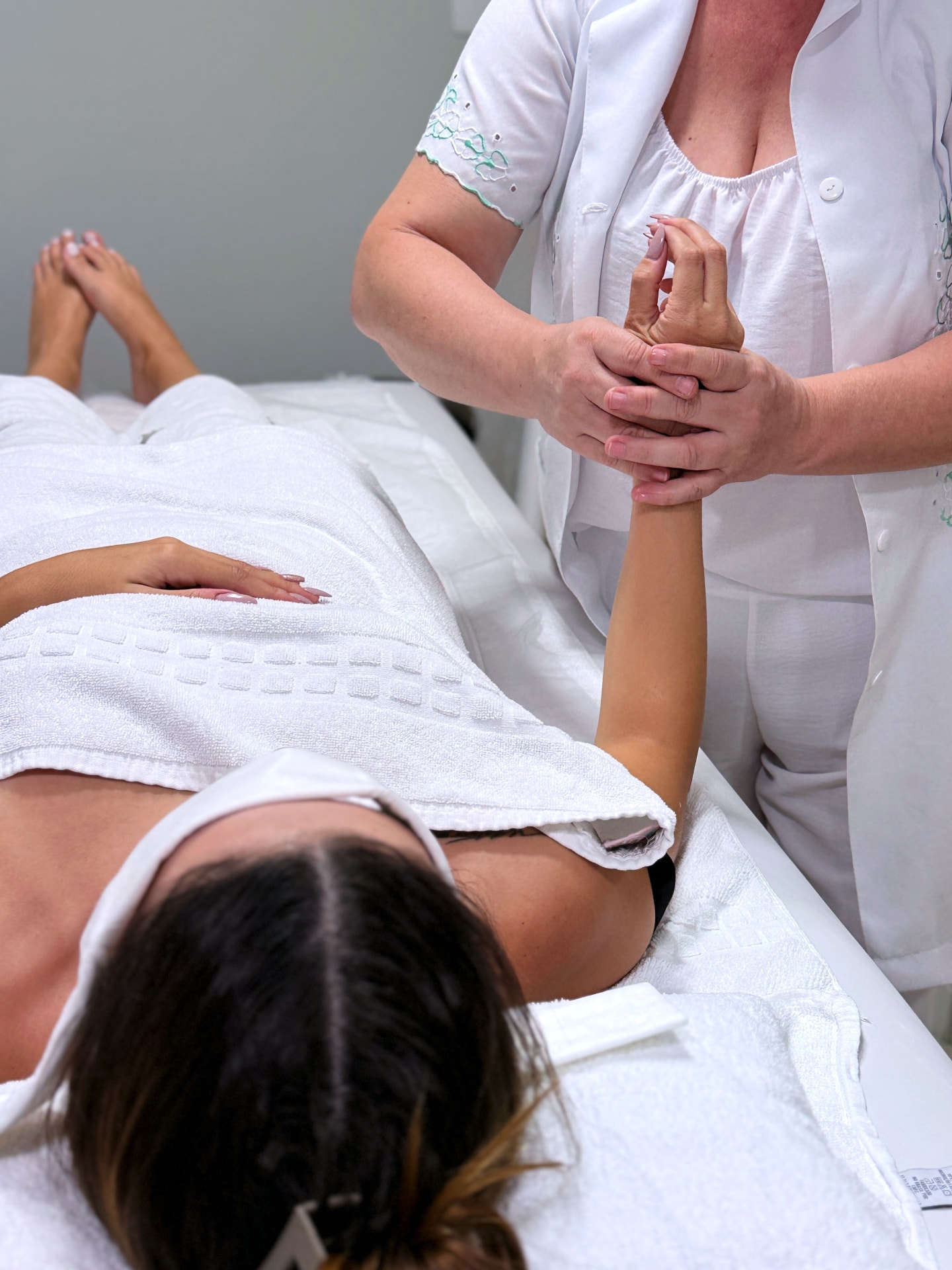Profissional de branco fazendo massagem na mão de cliente deitada na maca, coberta por toalhas brancas, no Nix Beauty Salon, no Shopping Palladium, em Curitiba
